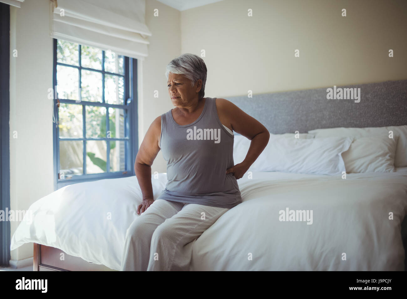 Senior woman suffering from back pain while sitting on bed at home ...