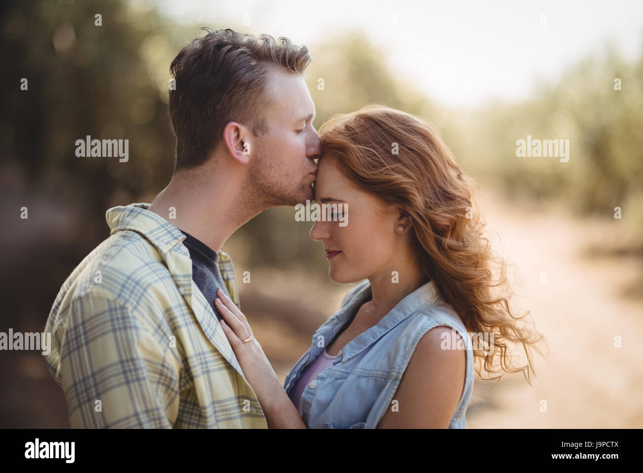 Side view of young man kissing woman at olive farm Stock Photo - Alamy