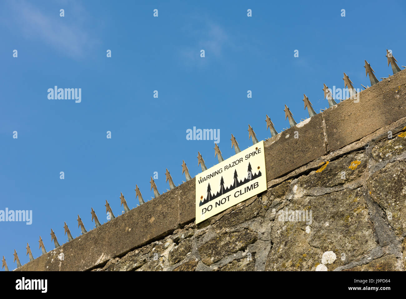 Razor spikes on the top of a stone wall with a sign warning do not climb. Stock Photo