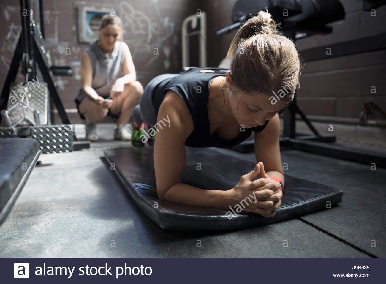Personal trainer timing female client doing plank exercise in gritty gym Stock Photo