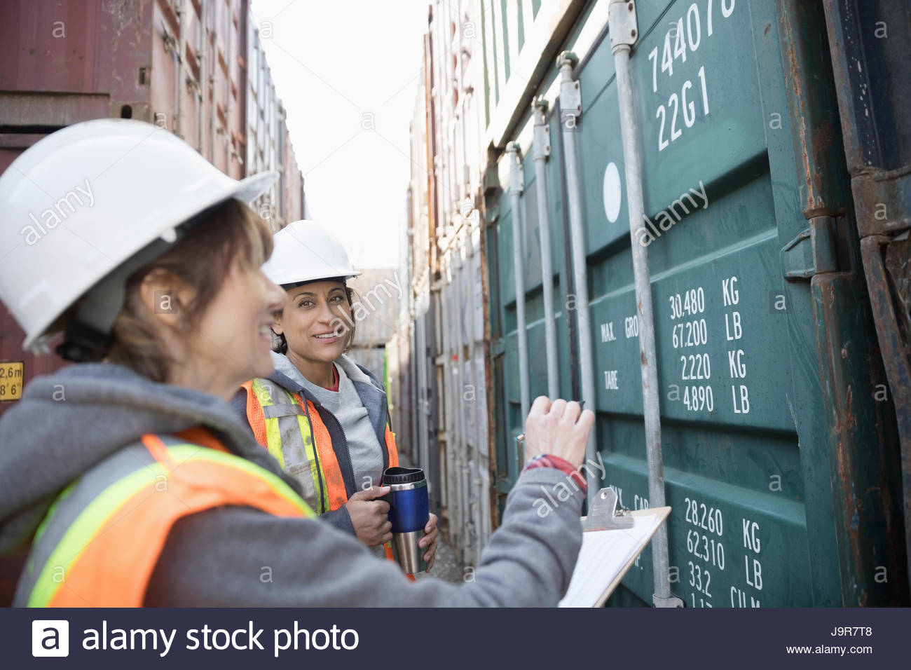 Female workers checking shipping containers in industrial container ...
