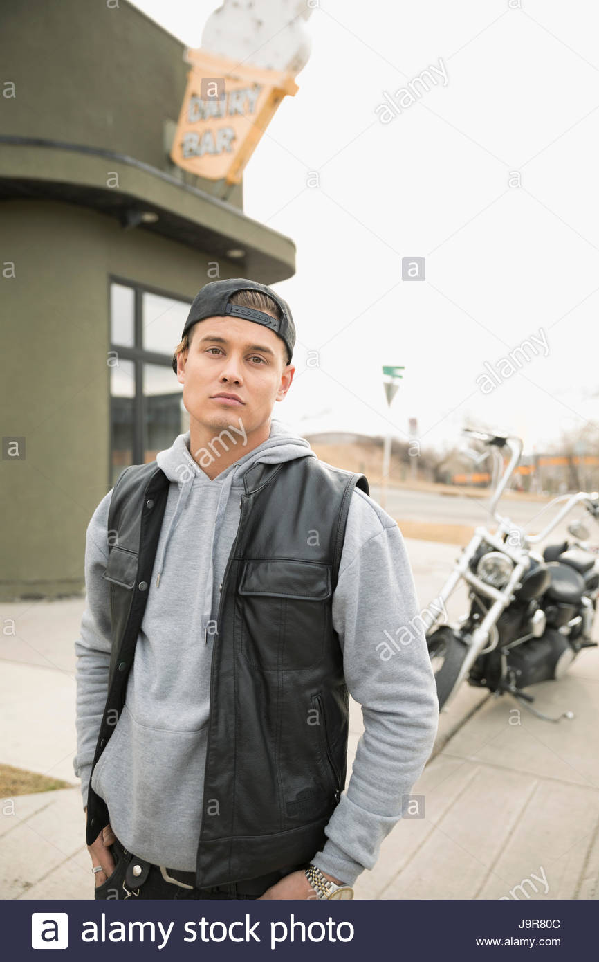 Portrait confident male biker in front of motorcycle in parking lot Stock Photo