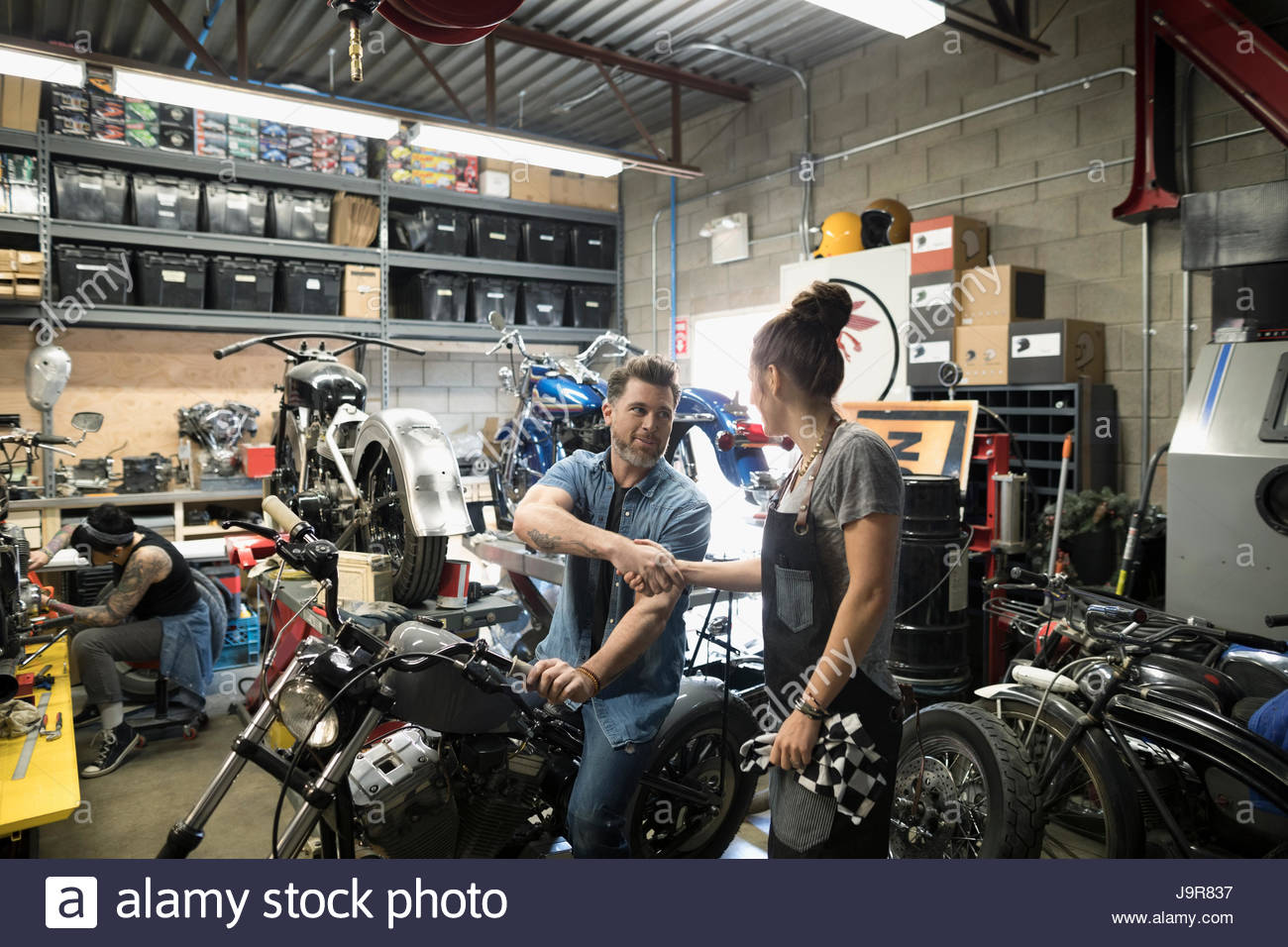 Male customer on motorcycle shaking hands with female mechanic in auto
