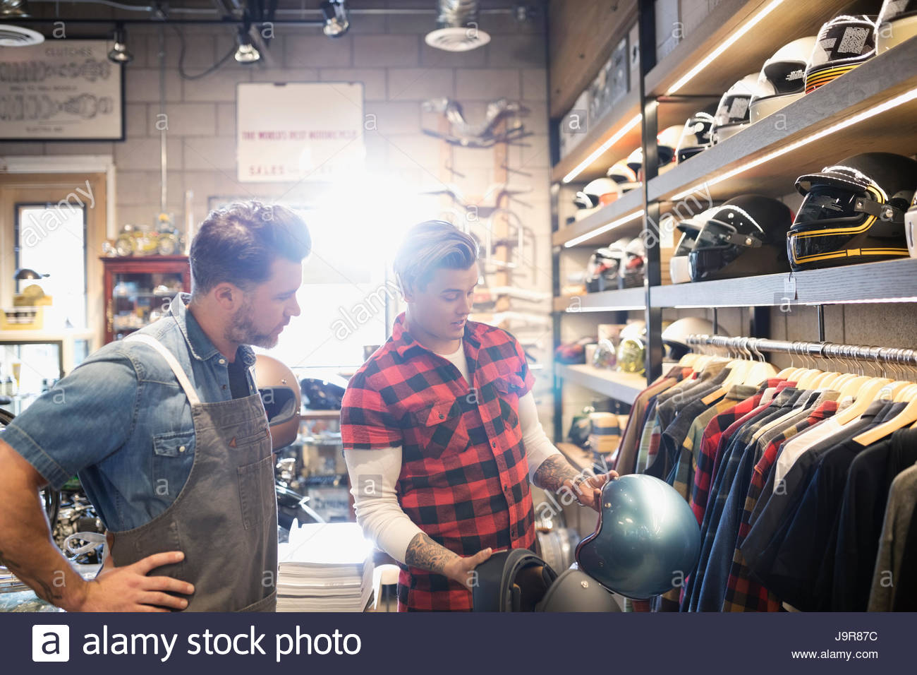 Motorcycle shop owner helping customer browsing helmets Stock Photo