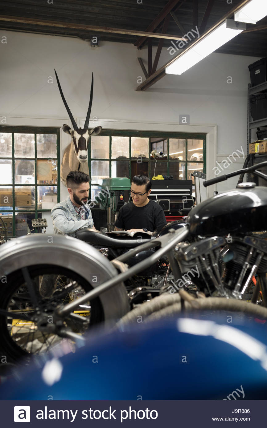 Motorcycle mechanics looking at part catalog in auto repair shop Stock