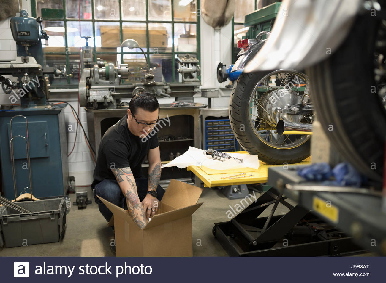 Motorcycle mechanic unpacking parts from cardboard box in auto repair ...