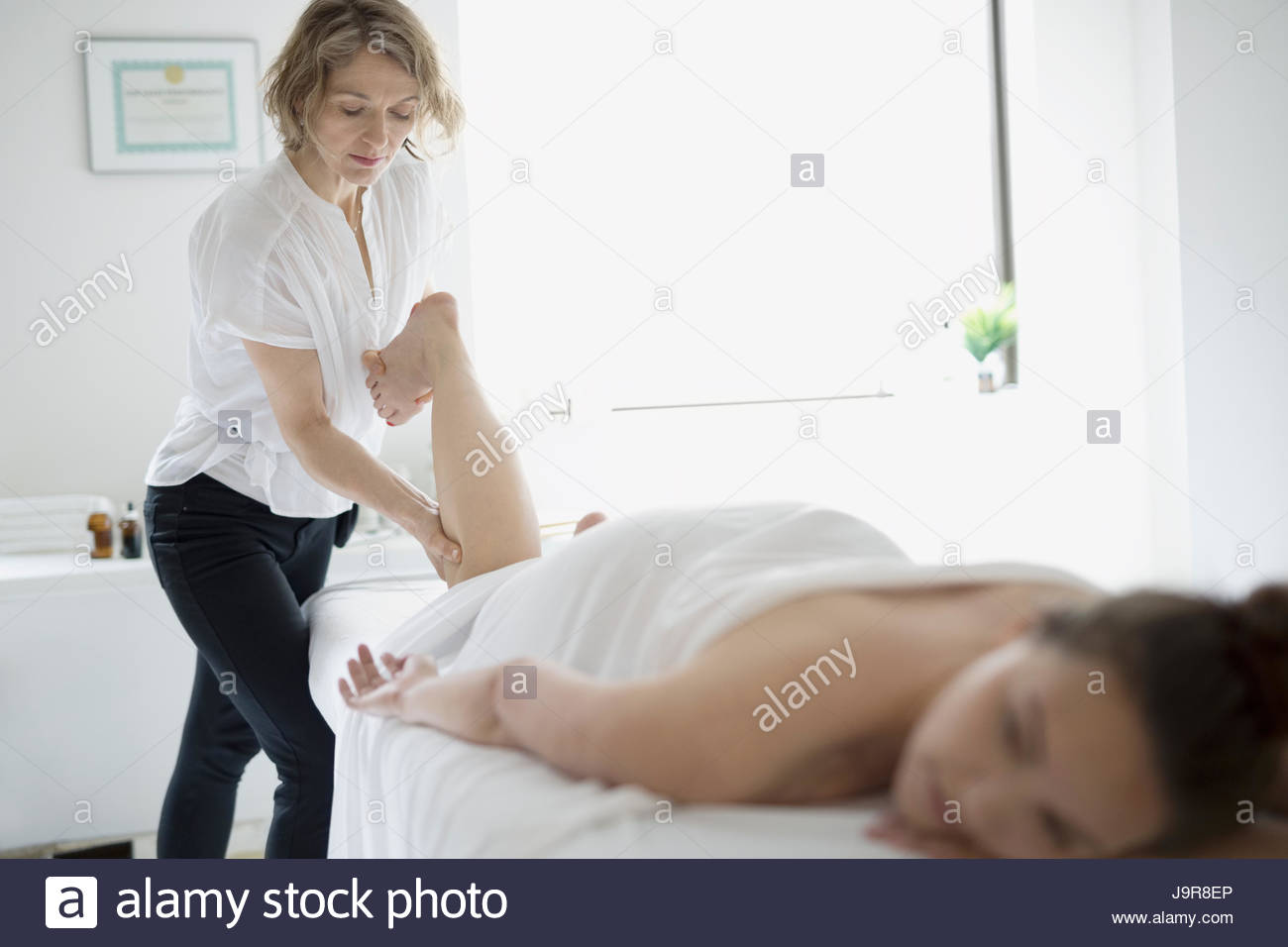 Masseuse massaging leg of woman on spa massage table Stock Photo