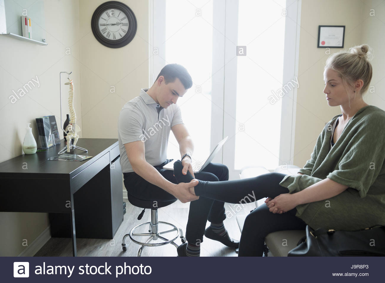 Male physiotherapist examining ankle of woman in clinic examination room Stock Photo