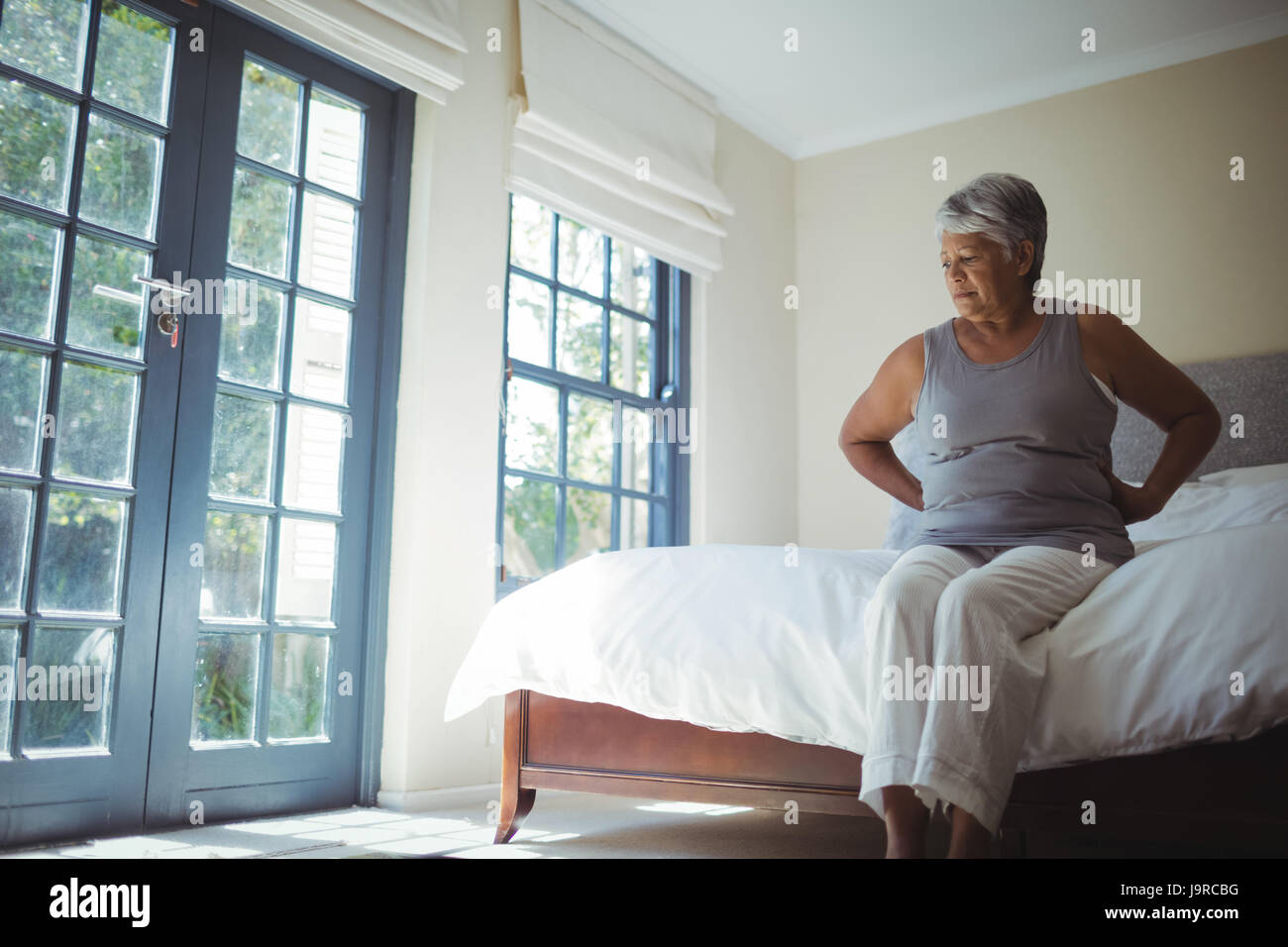 Senior woman suffering from back pain while sitting on bed at home ...