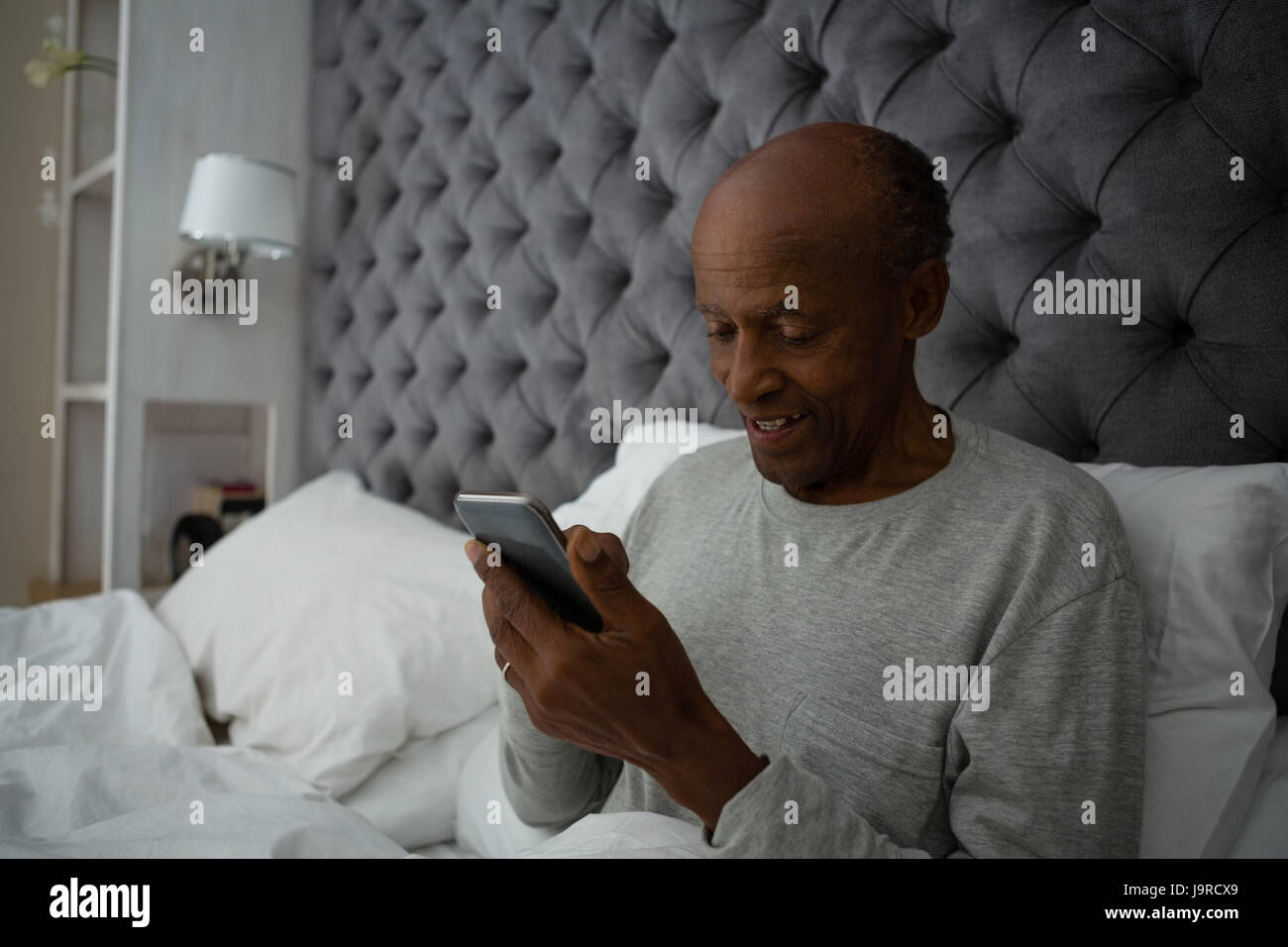 Senior man using mobile phone while sitting on bed at home Stock Photo ...