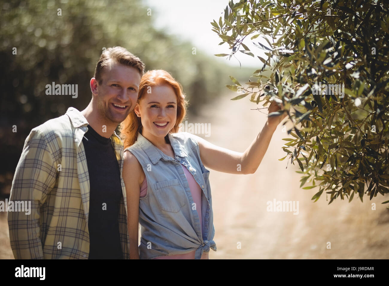 Portrait of smiling young couple standing by olive tree at farm Stock ...