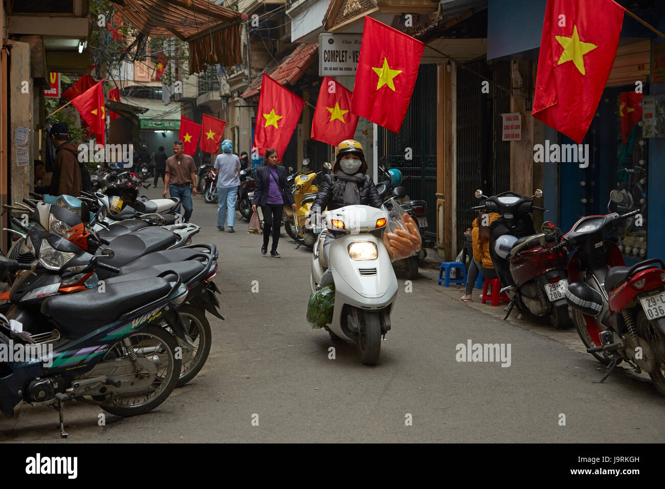 Vietnamese flags and woman riding scooter down alleyway, Old Quarter, Hanoi, Vietnam Stock Photo
