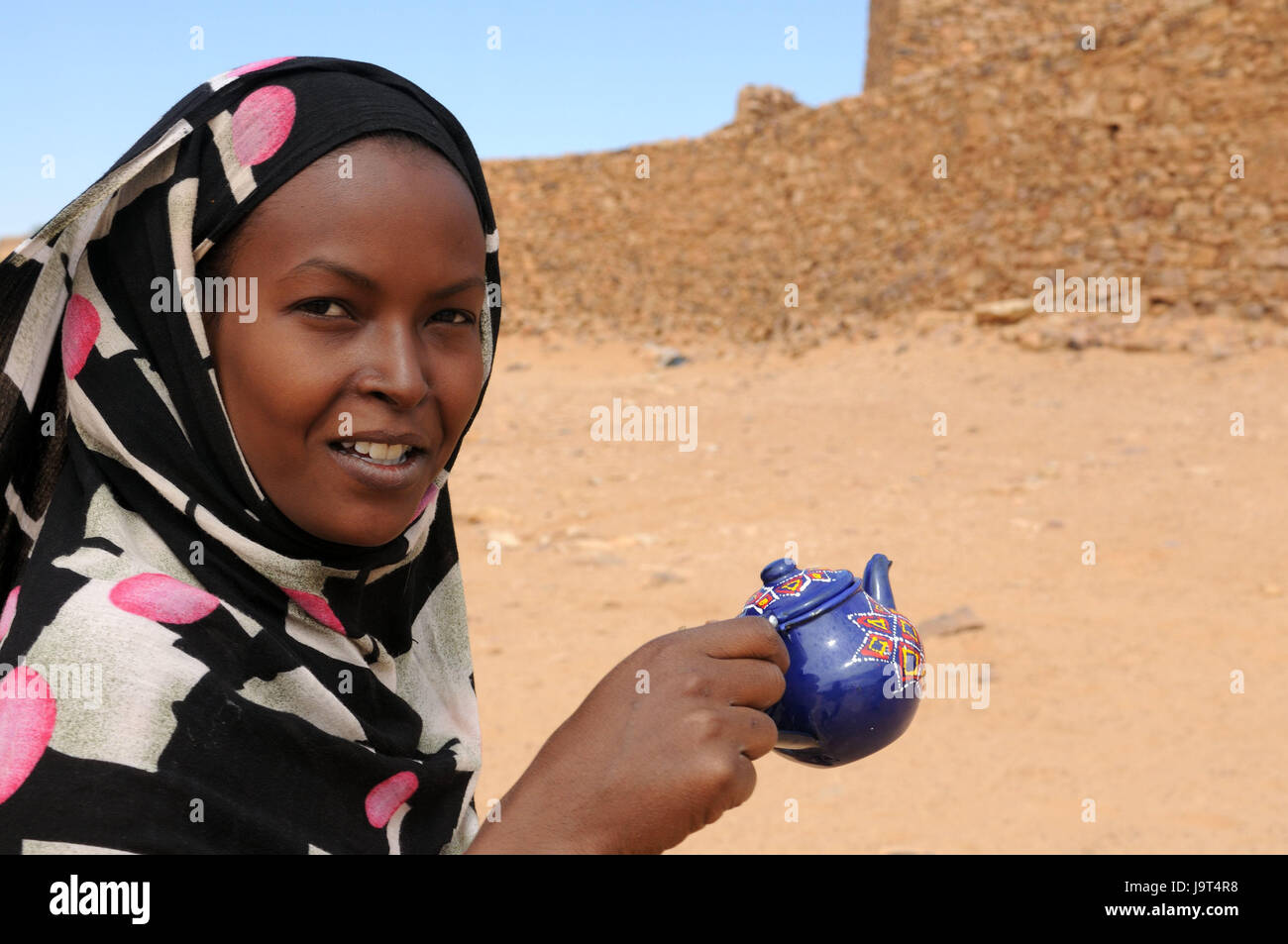Mauritania,Adrar,Ouadane,ruins,woman,headscarf,pot,hold,portrait,no model release,Africa,West Africa,town,wild town,oasis town,destination,historically,culture,architecture,defensive walls,Sand,UNESCO-world cultural heritage,place of interest,outside,people,locals,non-whites,headgear,friendly,teapot, Stock Photo