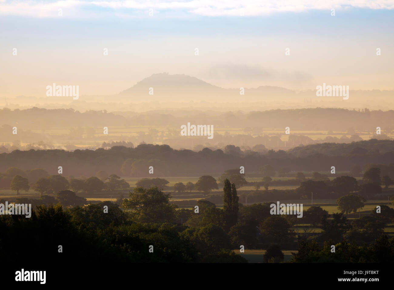 A misty rural landscape in summer across the Cheshire Plain towards Beeston Castle on the prominet hill overlooking the landscape, Cheshire, England, UK Stock Photo