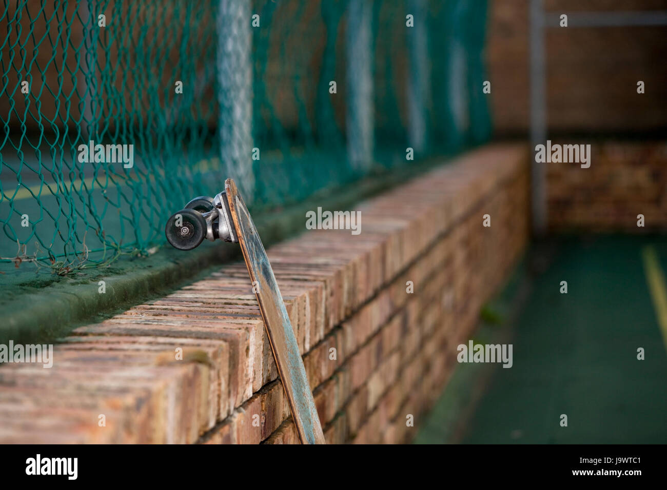 Skateboard leaning against a brick wall in tennis court yard Stock