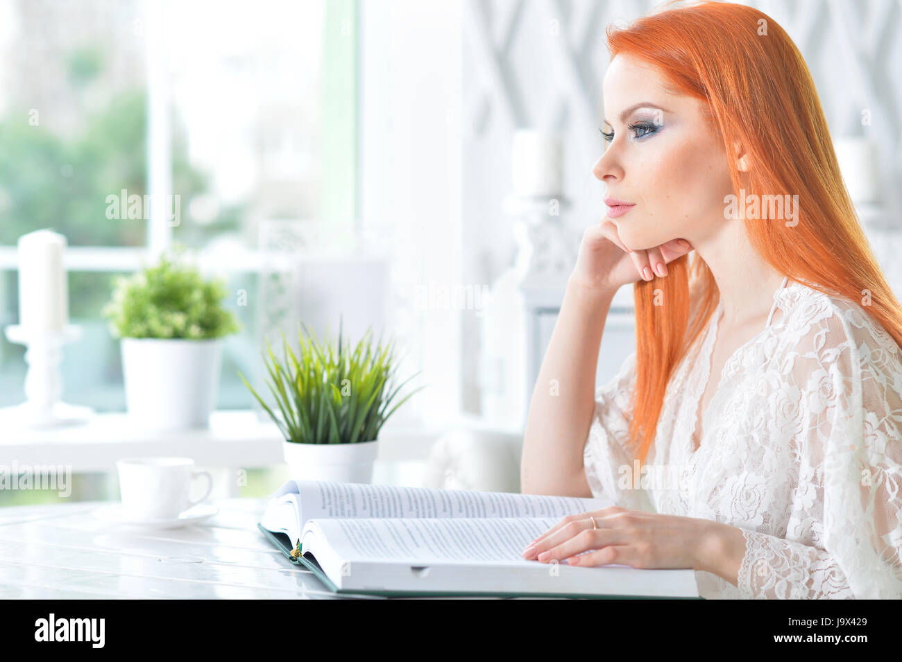Beautiful girl reading a book while sitting at a table Stock Photo - Alamy
