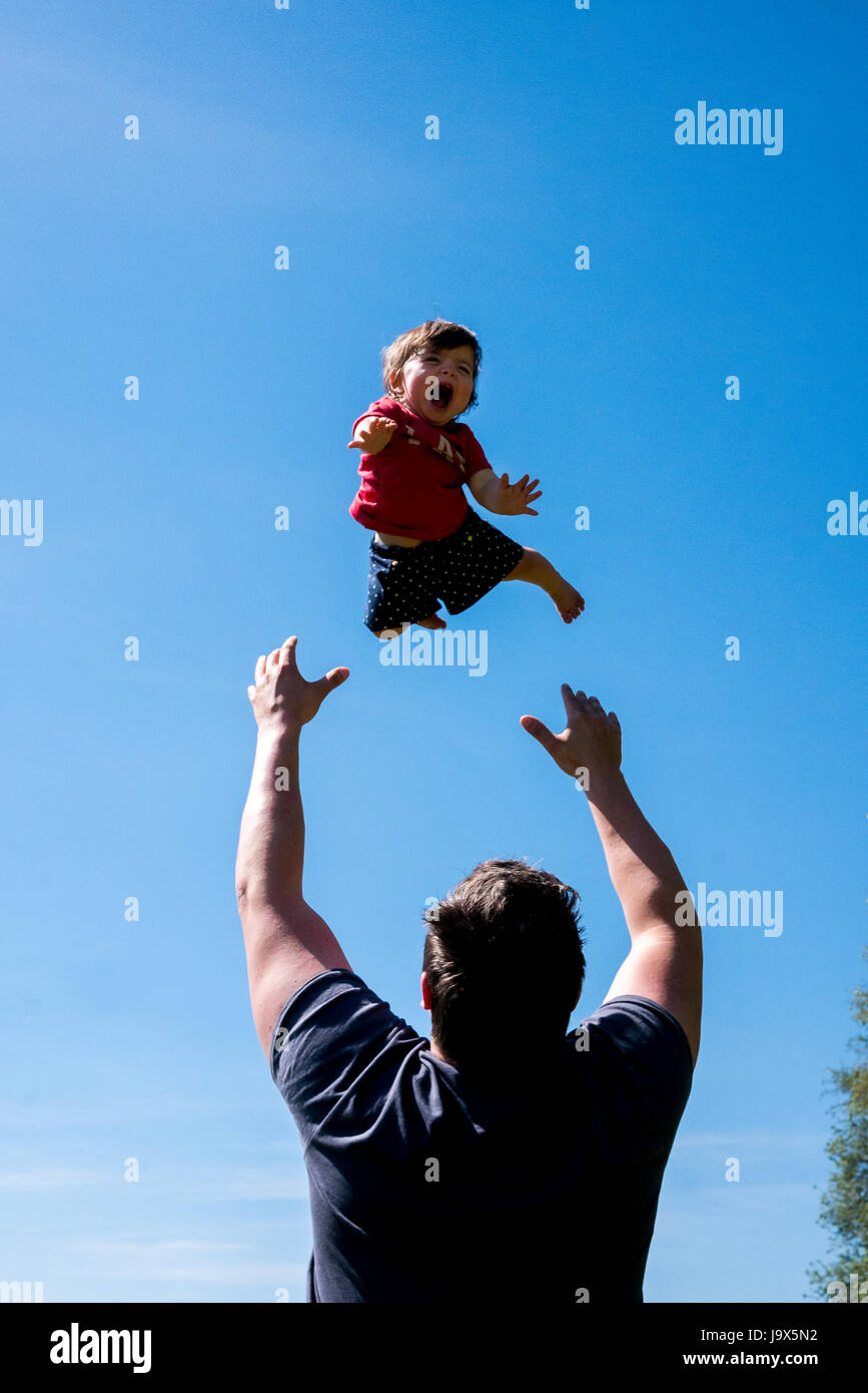 A happy child been thrown up in the air by daddy against a blue sky