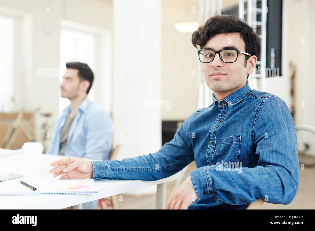 Young man in eyeglasses sitting by desk at lesson Stock Photo