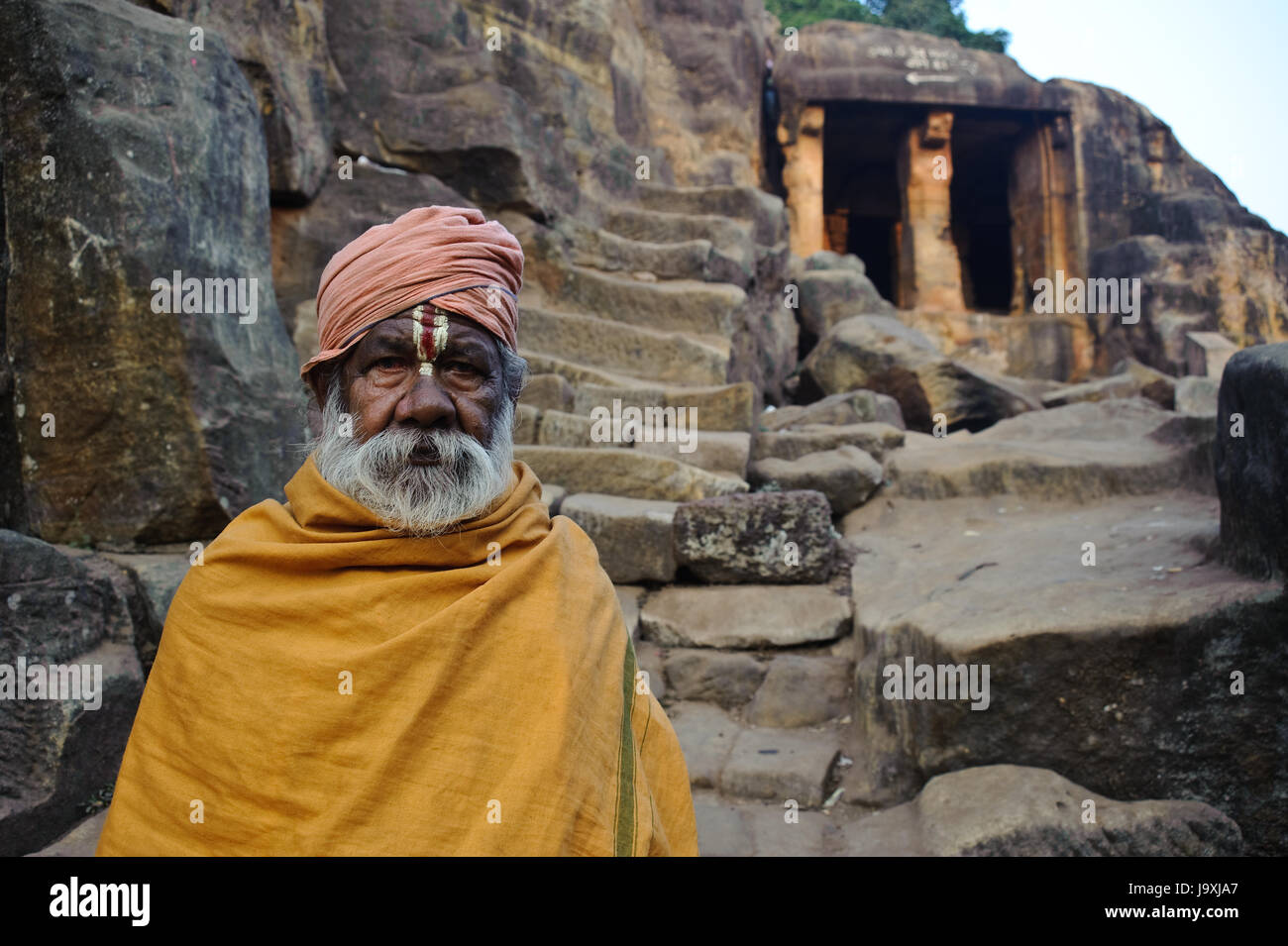 Hindu ascetic ('sadhu') standing in front of a cave ( Khandagiri, India). Him and other persons are staying in such caves. Stock Photo