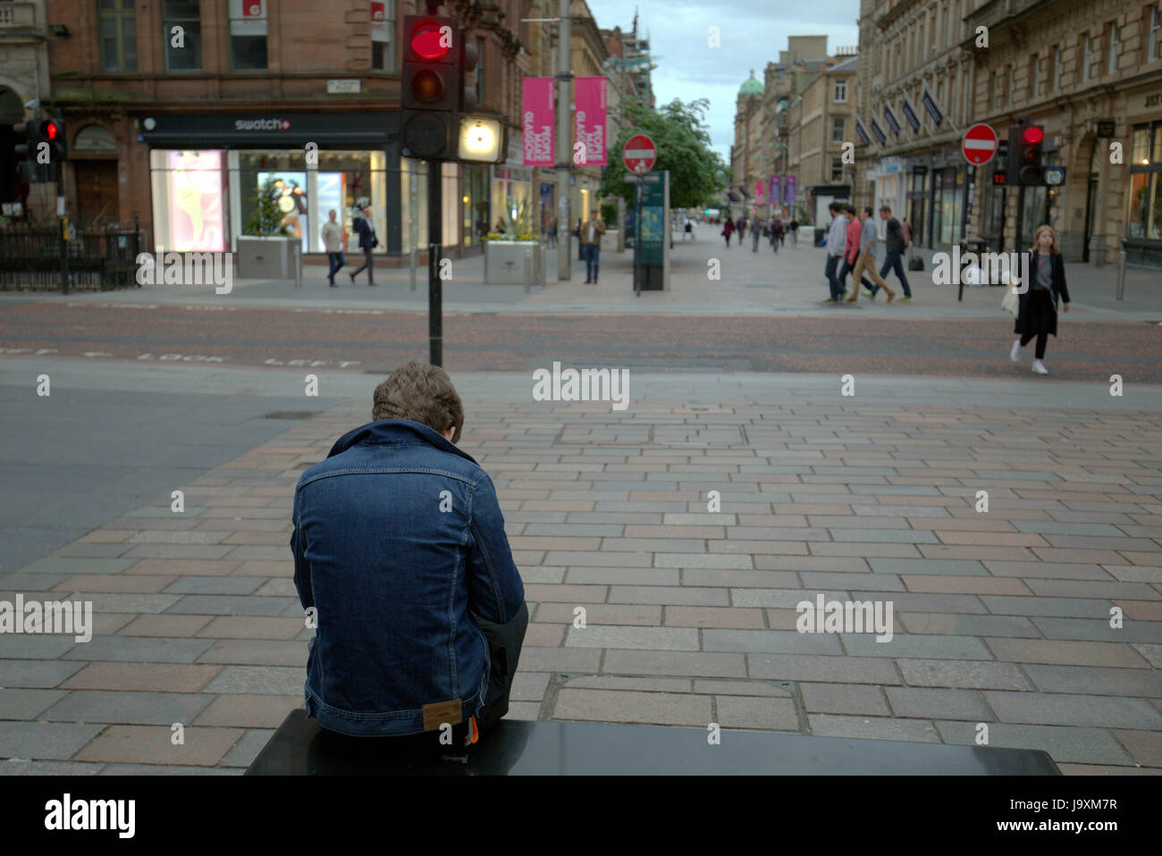 teenage boy sitting alone in a shopping street at night Buchanan St, Glasgow Stock Photo