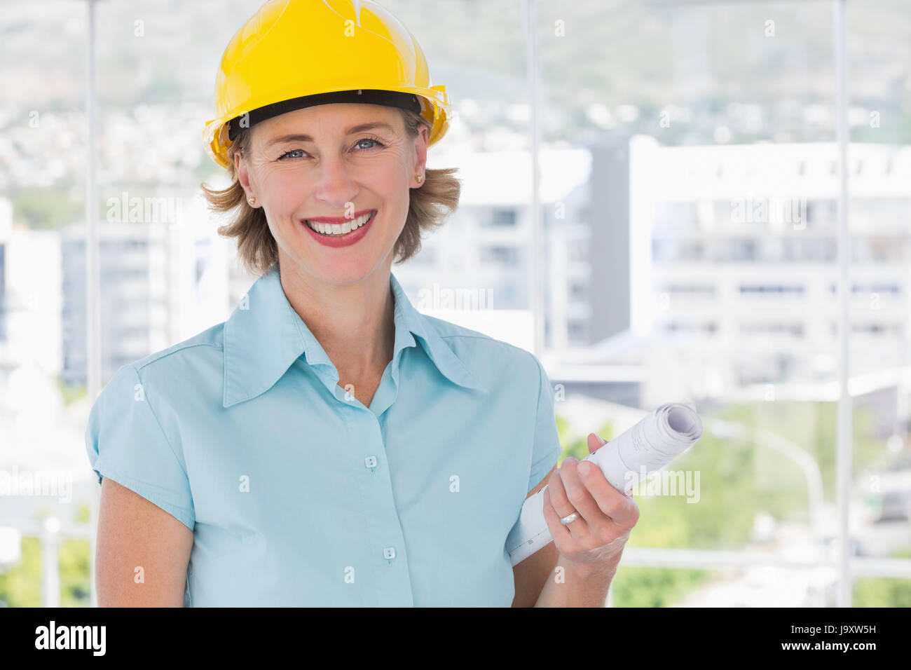 Smiling architect looking at camera with helmet and blueprint Stock ...