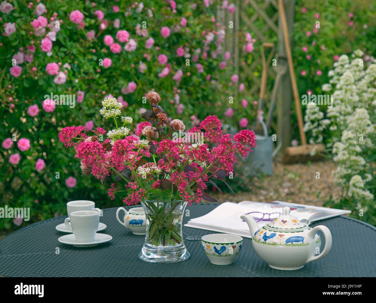 Red Valerian, climbing roses and tea table in garden still life Stock Photo