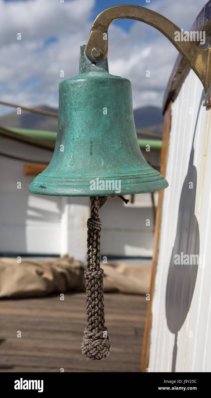 Brass ship's bell onboard an old sailing ship with a remote Scottish island in the background Stock Photo
