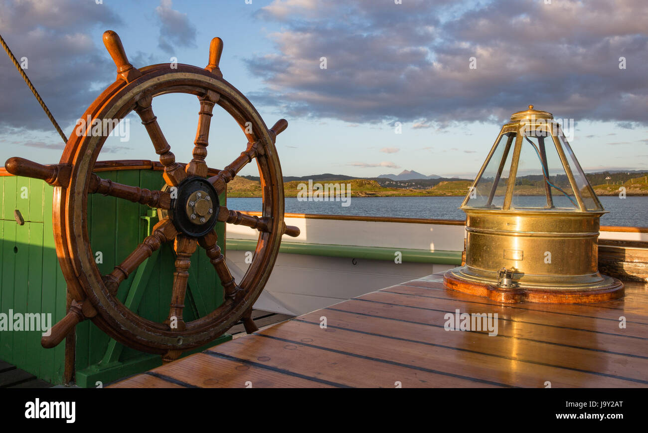 Ship's wheel and compass binnacle onboard an old sailing ship, taken late in the evening in a soft golden light, looking towards Kerrera in Scotland Stock Photo