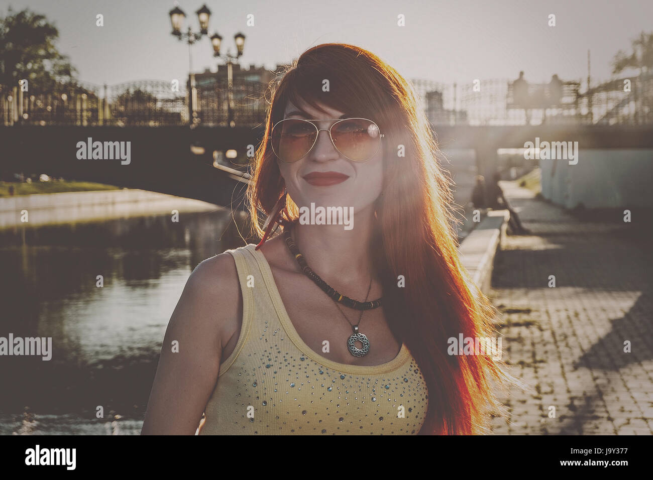 Head and shoulders of ginger hair woman in orange color sunglasses backlit vintage color grading Stock Photo