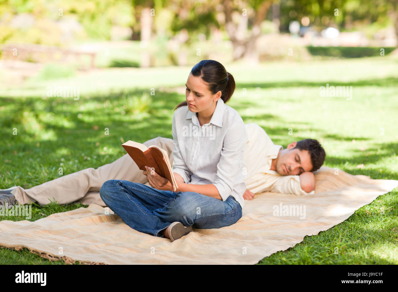 Woman reading while her husband is sleeping in a park Stock Photo Alamy