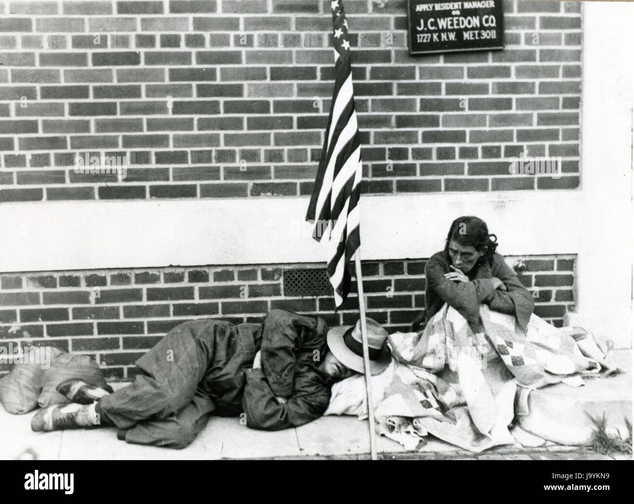 Washington, D.C., July, 1932 - World War I veteran and his wife rest on a sidewalk under their flag and blankets where they slept after being evicted by troops from their shantytown with other Bonus Marchers. Stock Photo