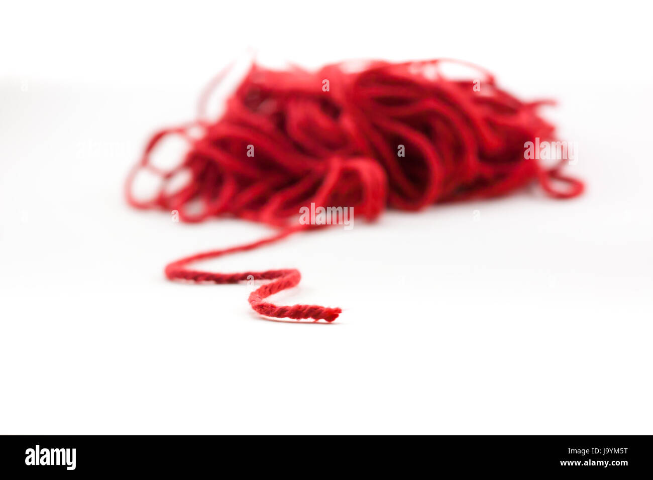 Tangled pile of red yarn with a single piece leading out, isolated on white. Stock Photo
