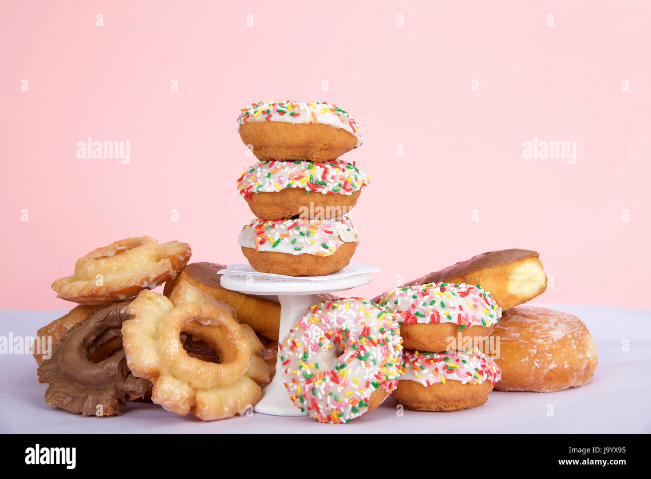 Cake donuts with white frosting and colorful sprinkles stacked on and around a small pedestal surrounded by birthday presents. Number 1 candle burning Stock Photo