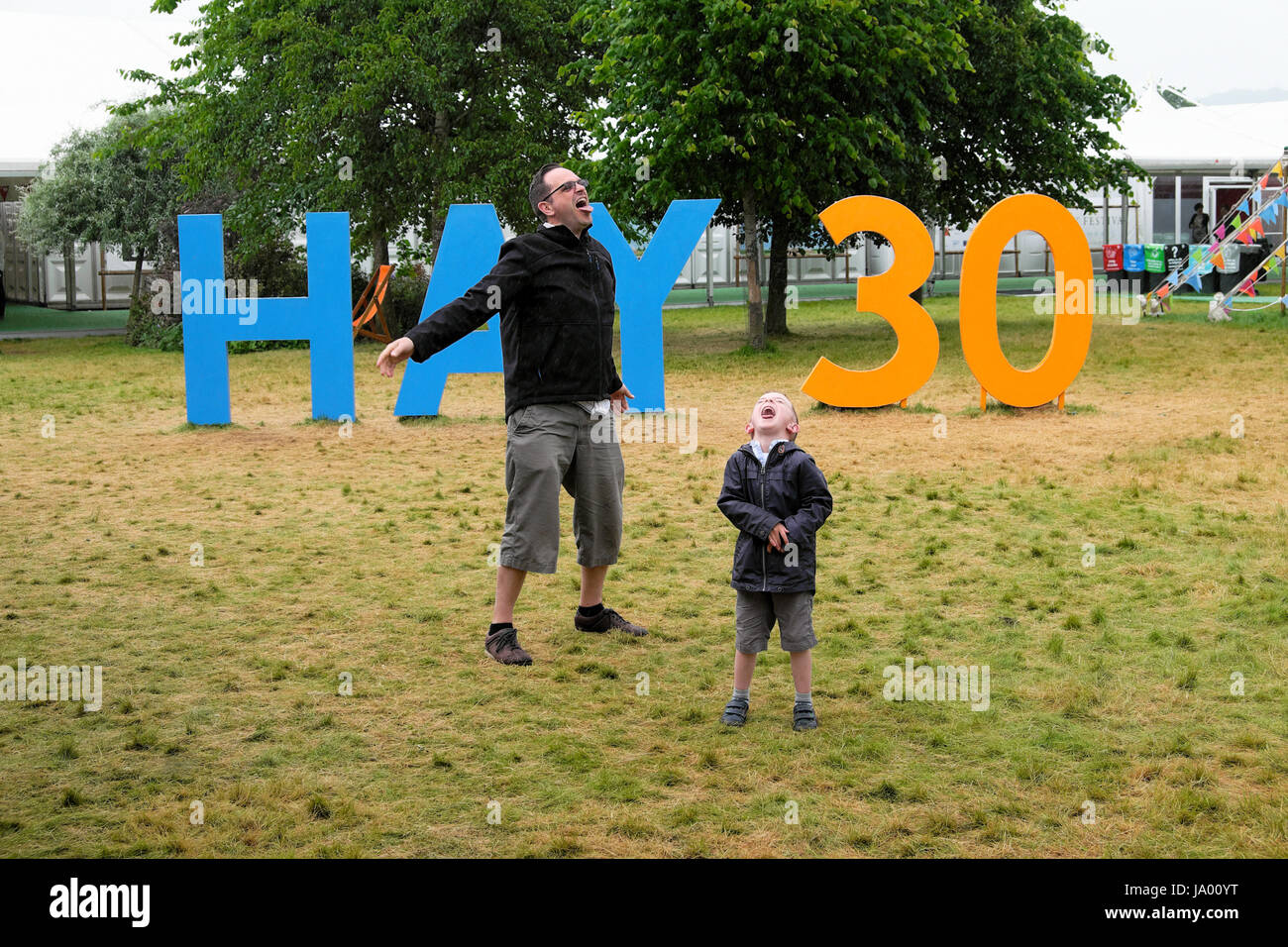 A father and son playing in front of the Hay 30 anniversary sign catch rain in open mouths at the 2017 Hay Festival Hay-on-Wye Wales UK   KATHY DEWITT Stock Photo