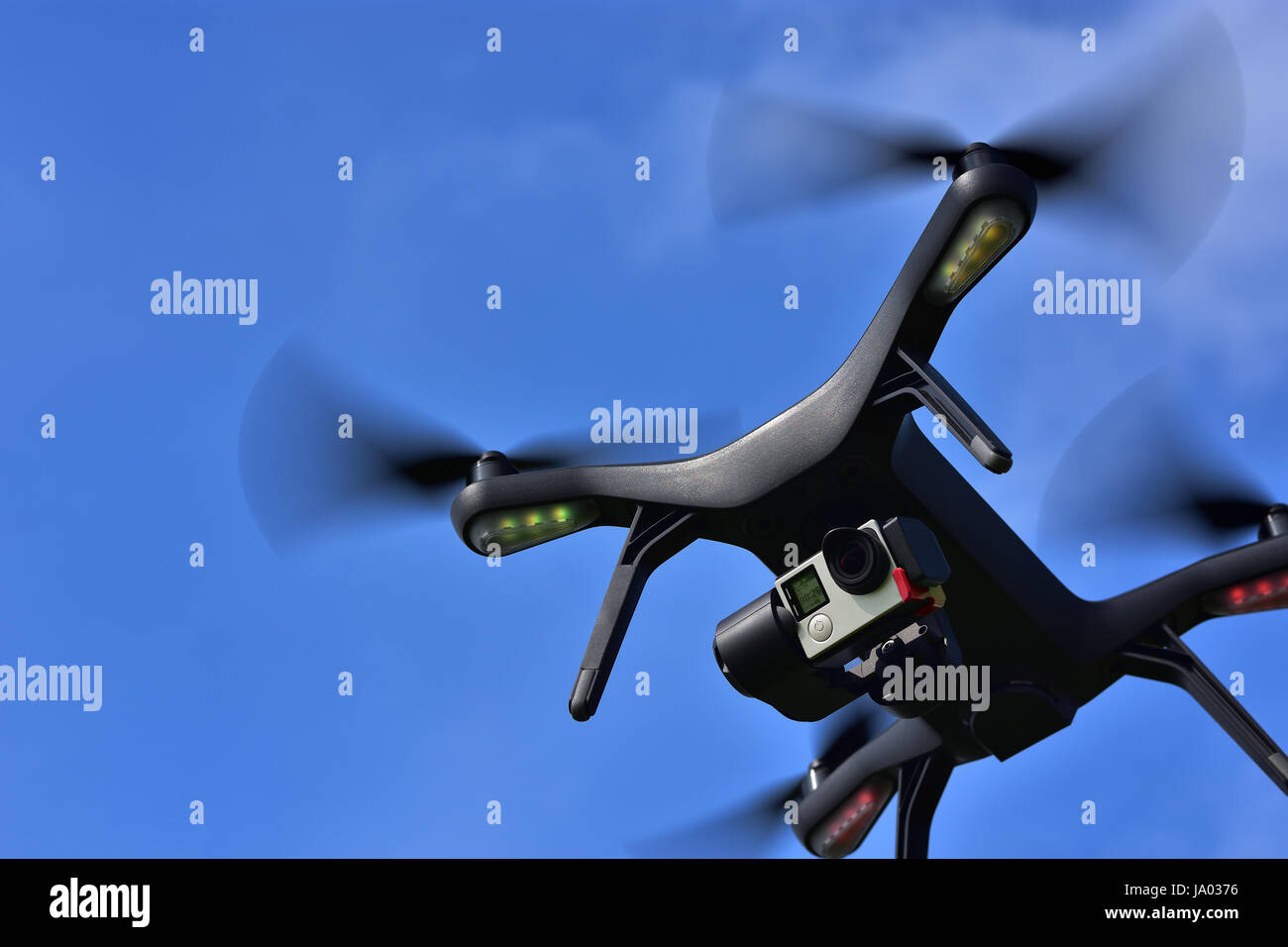 Black drone with camera flying over blue sky. Angle view, copy space. Stock Photo