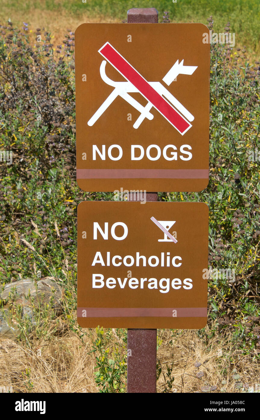Brown signs, no dogs and no alcoholic beverages. Tall weeds growing in background. Stock Photo