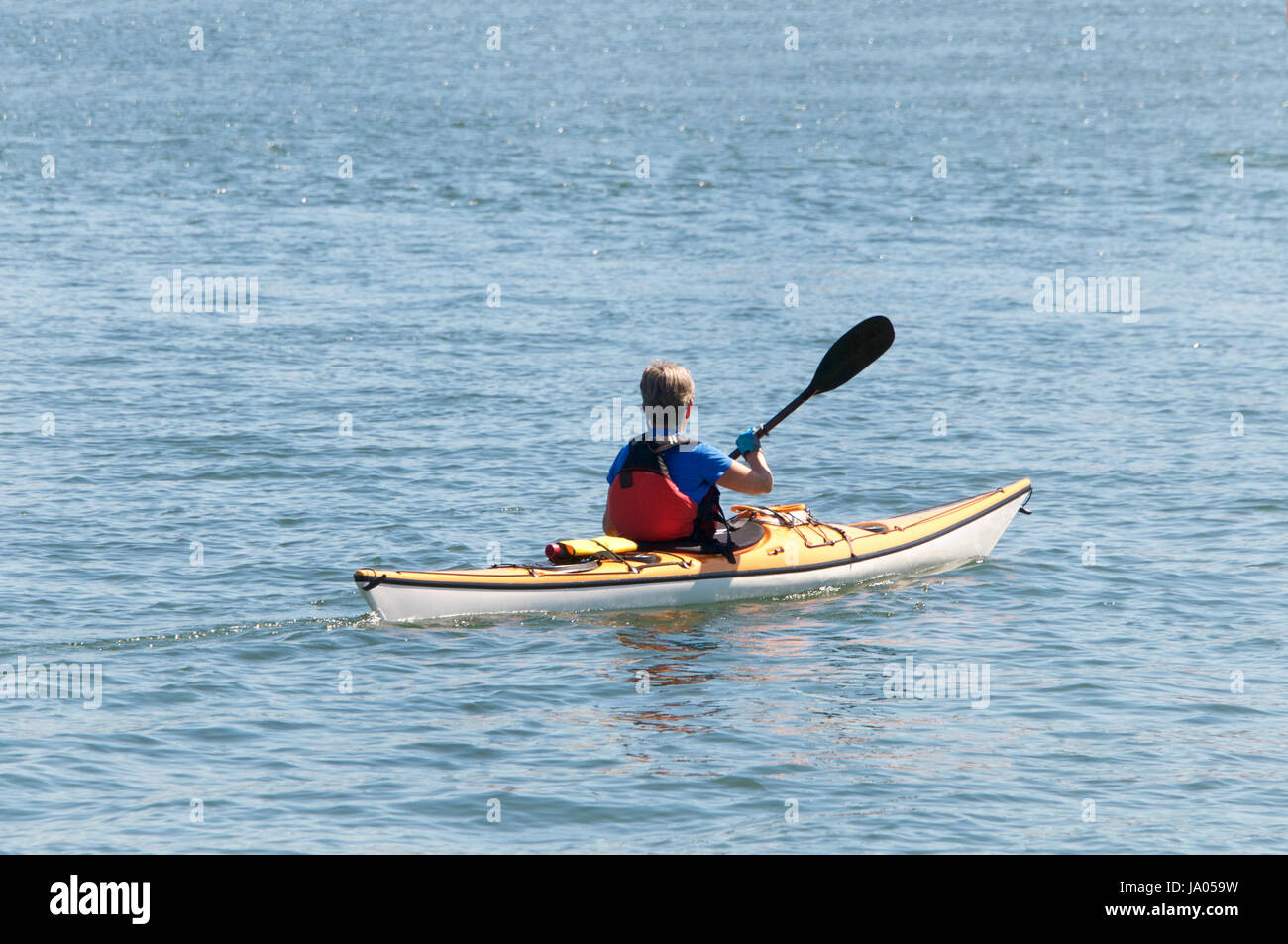 Lone kayak with older female paddling in open water away from viewer Stock Photo