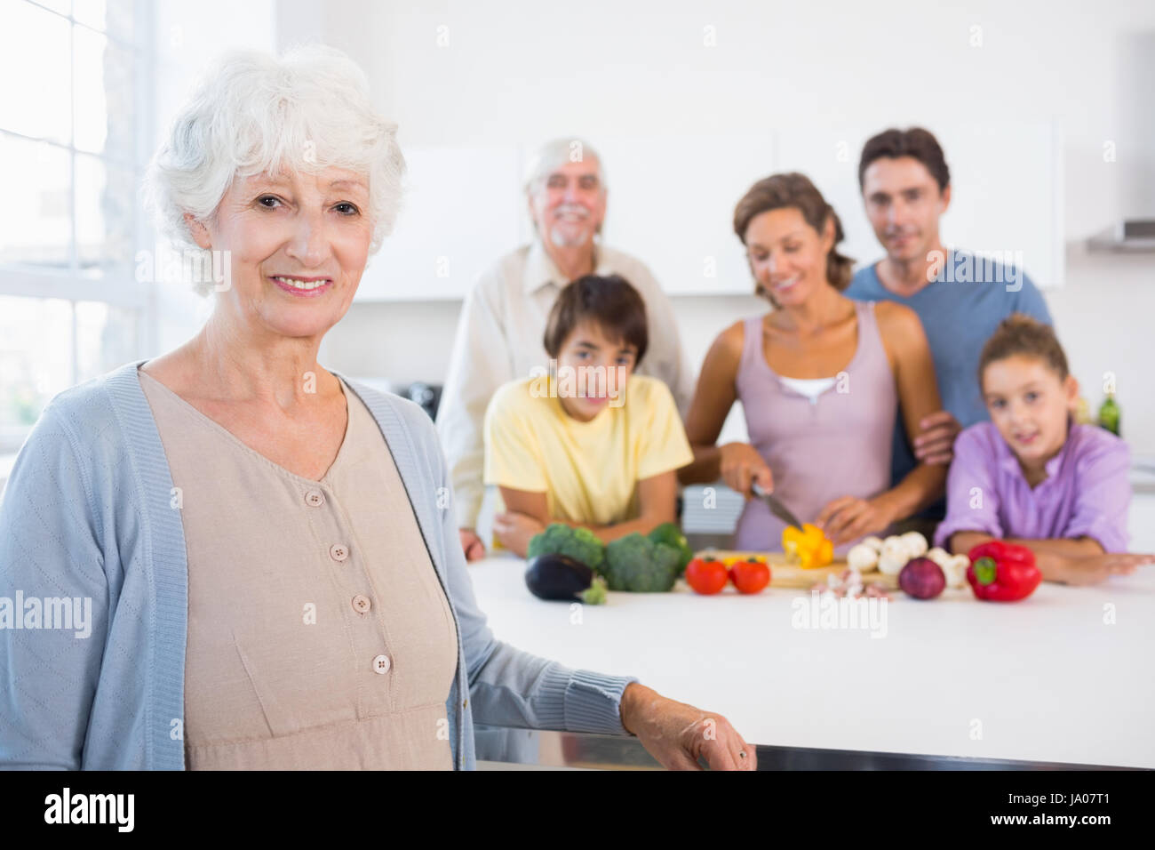 Grandmother standing beside kitchen counter with family behind her ...