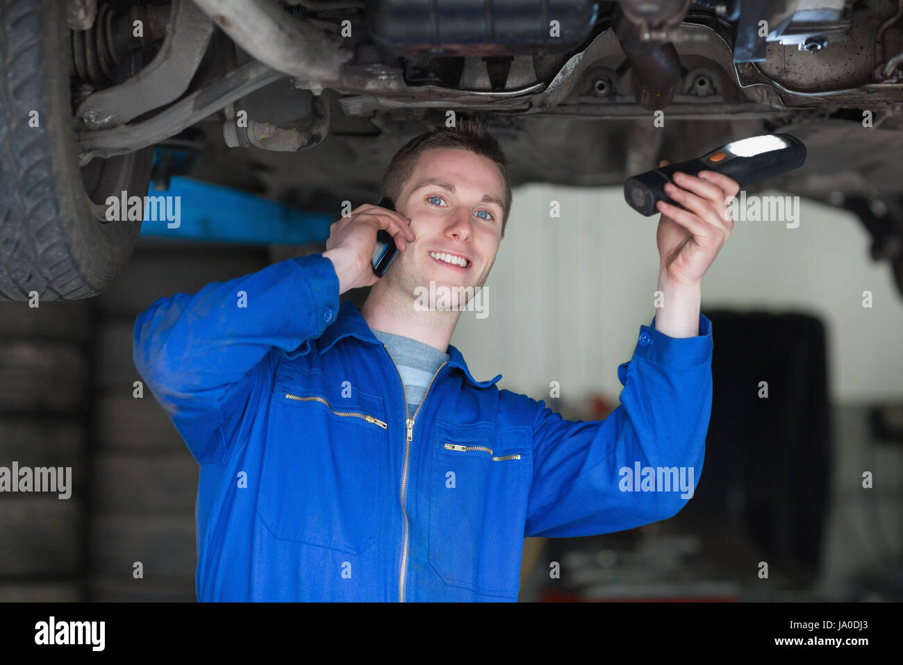Portrait of mechanic using cell phone as he stands under car Stock Photo