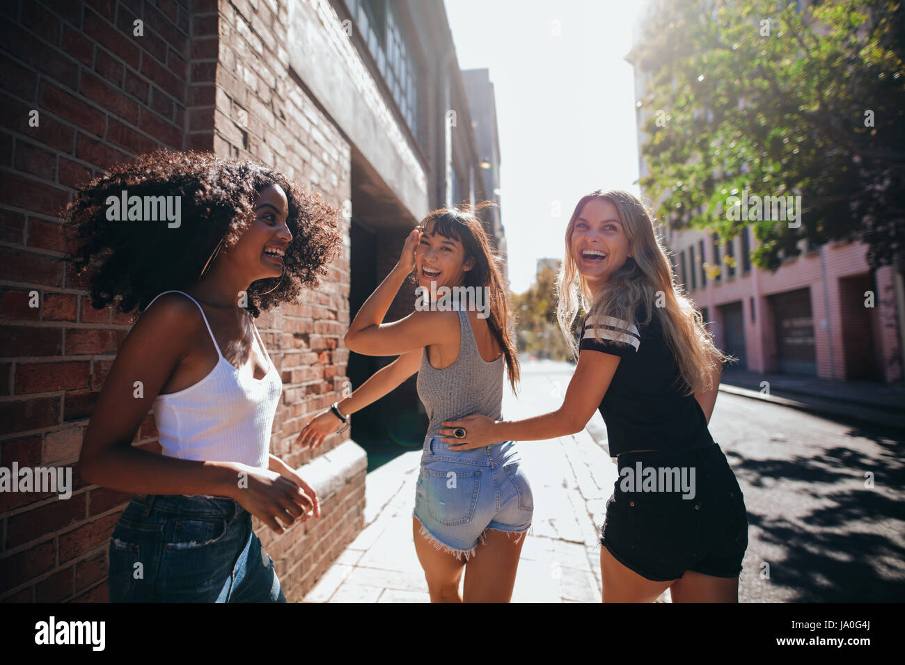 Mixed raced group of friends walking together in city. Three young people having fun outdoors on road. Stock Photo