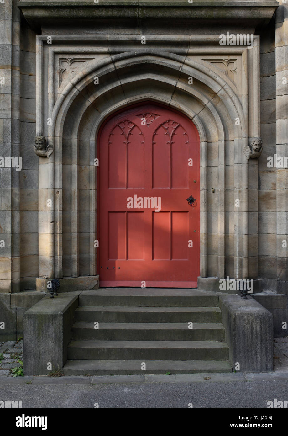 Arched stone church door surround with red wooden door and stone steps at all saints church stand whitefield bury lancashire uk Stock Photo