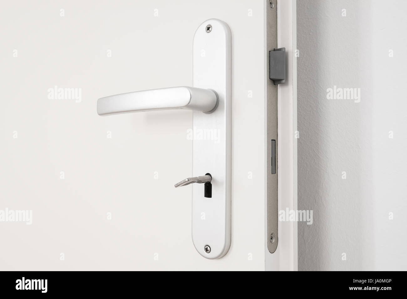 metallic door handle with key on white door closeup Stock Photo