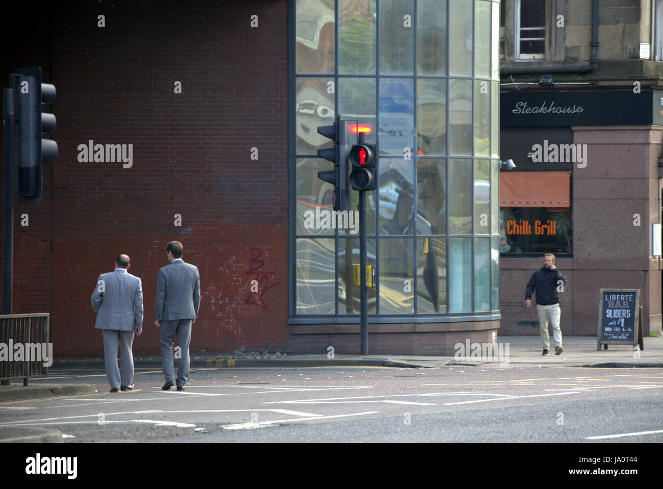 two men in gray suits on the street at red traffic light Charing Cross Glasgow Stock Photo