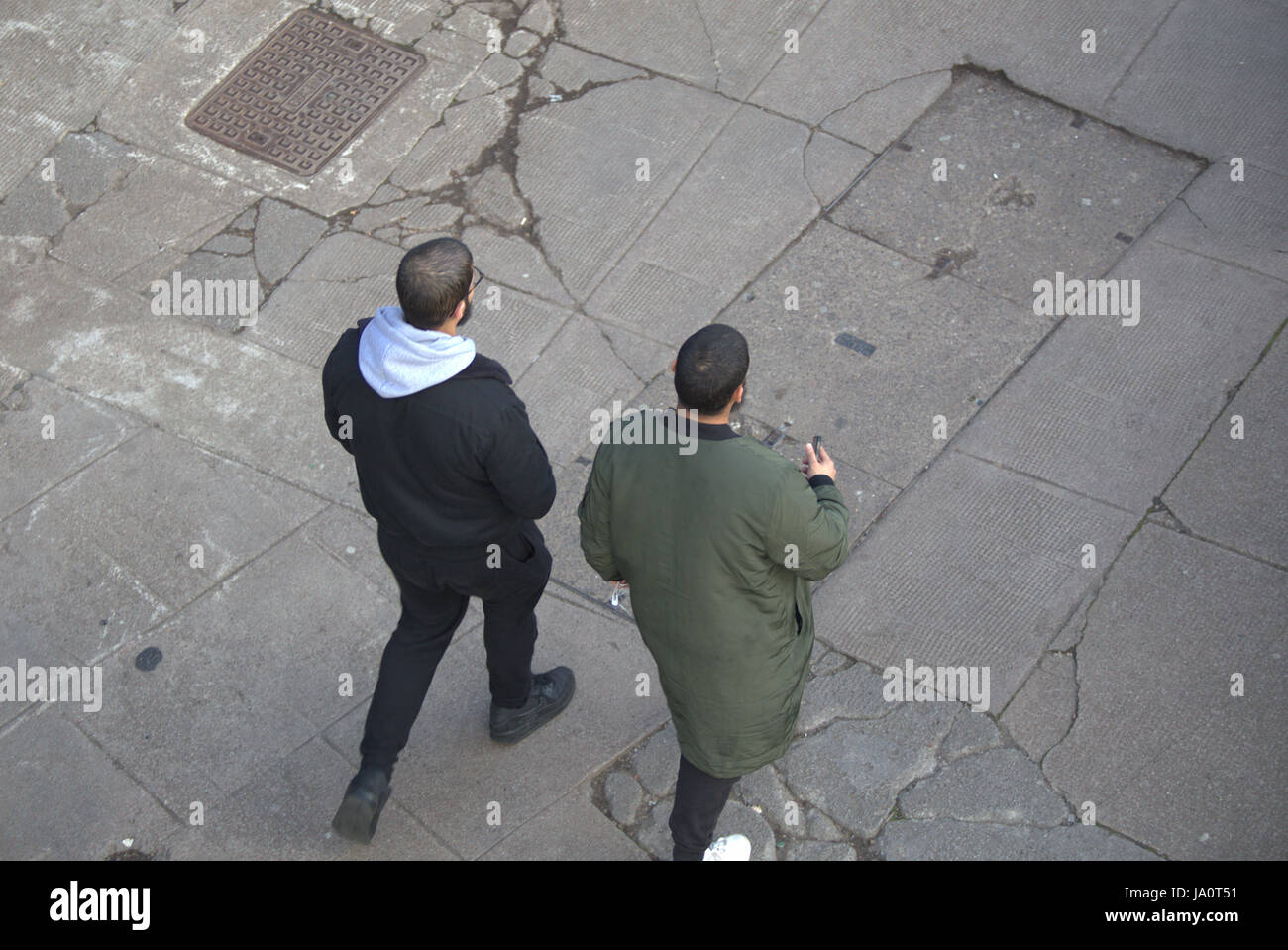 two young Asian or Arab men males walking on cracked concrete pavement Stock Photo