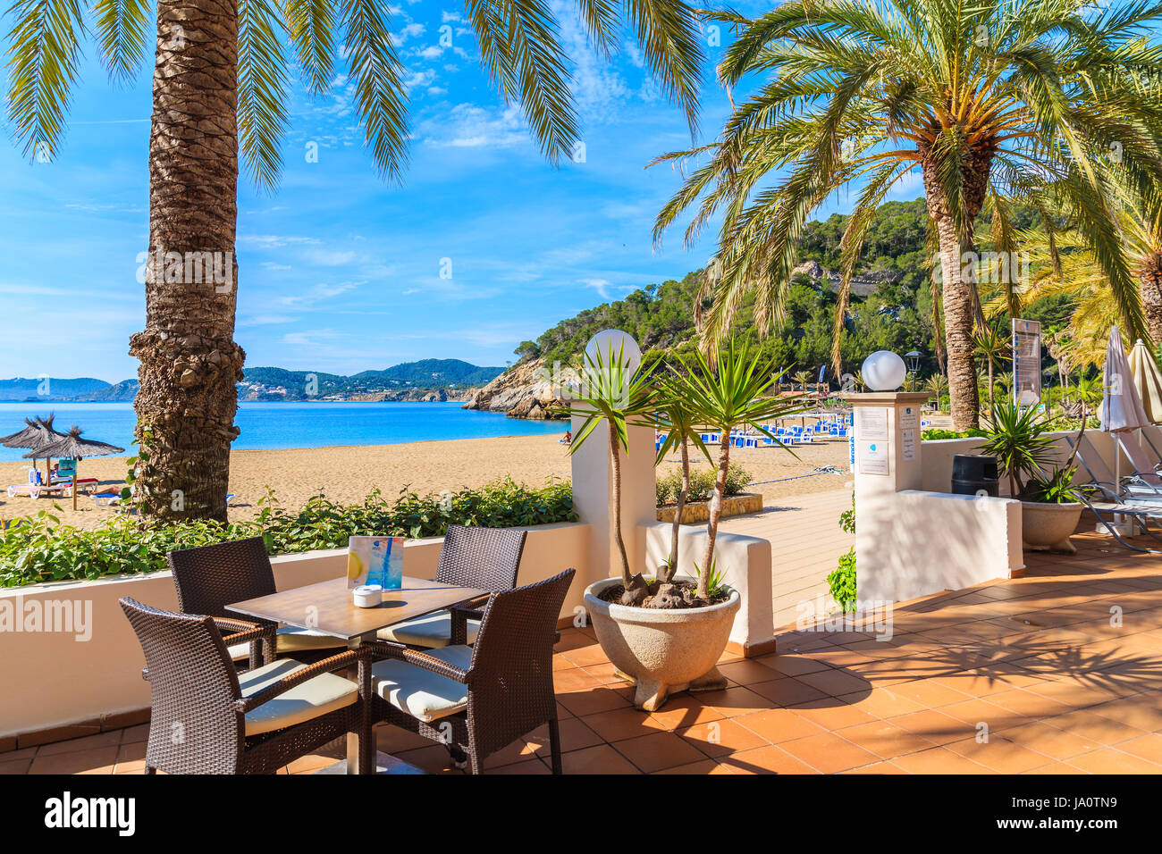 CALA SAN VICENTE BAY, IBIZA ISLAND - MAY 17, 2017: Hotel bar tables on beach with palm trees in Cala San Vicente bay, Ibiza island, Spain. Stock Photo