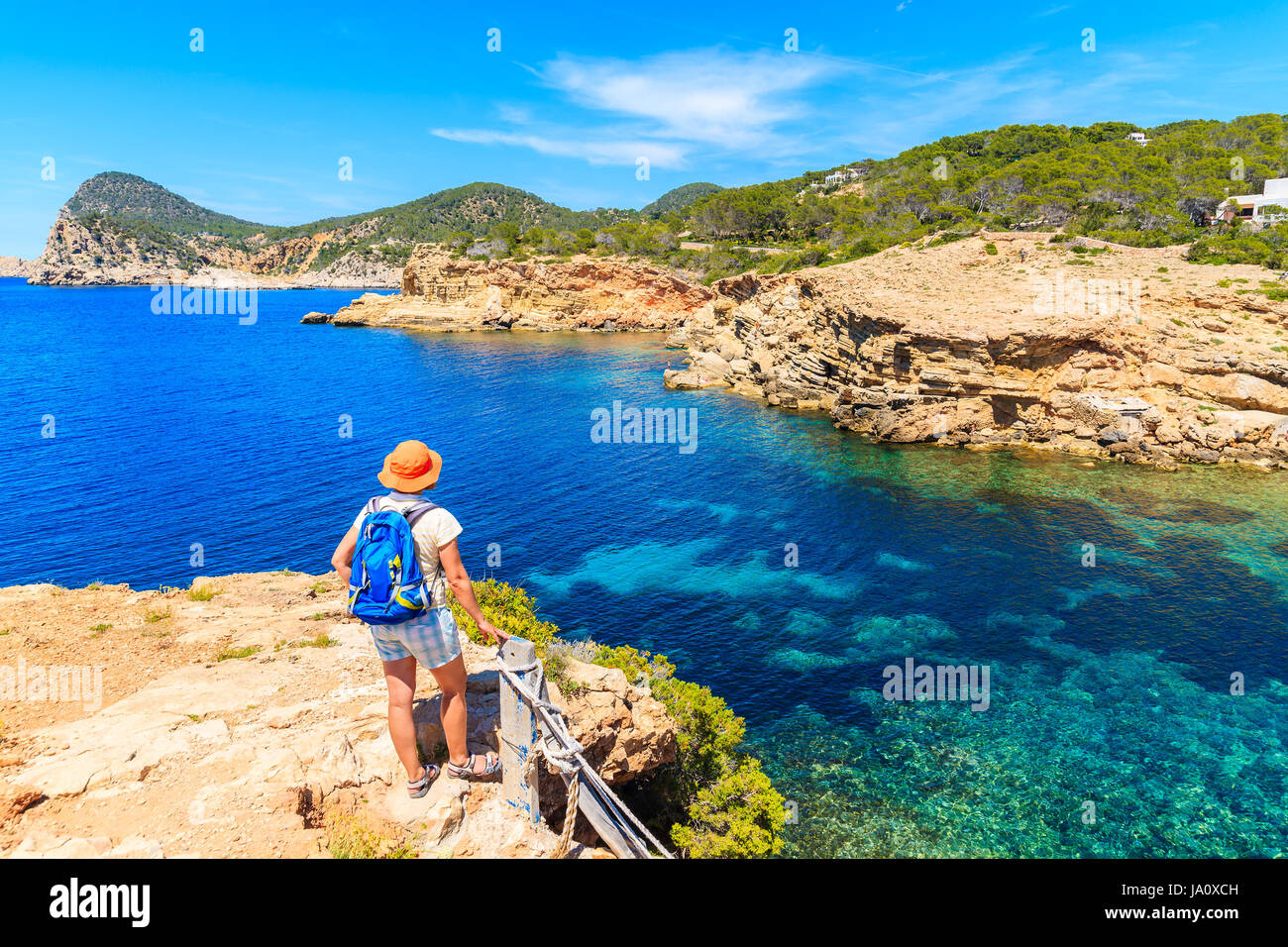 Young woman tourist backpacker standing on cliff and looking at Punta Galera bay surrounded by amazing stone formations, Ibiza island, Spain Stock Photo