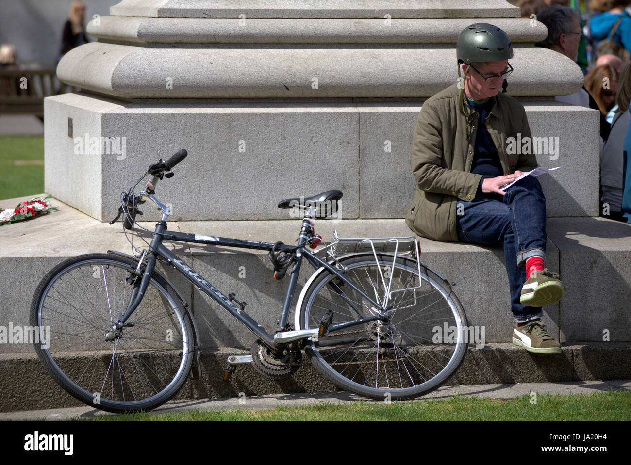 cyclist sitting down reading map with bike against monument in George Square Glasgow Stock Photo