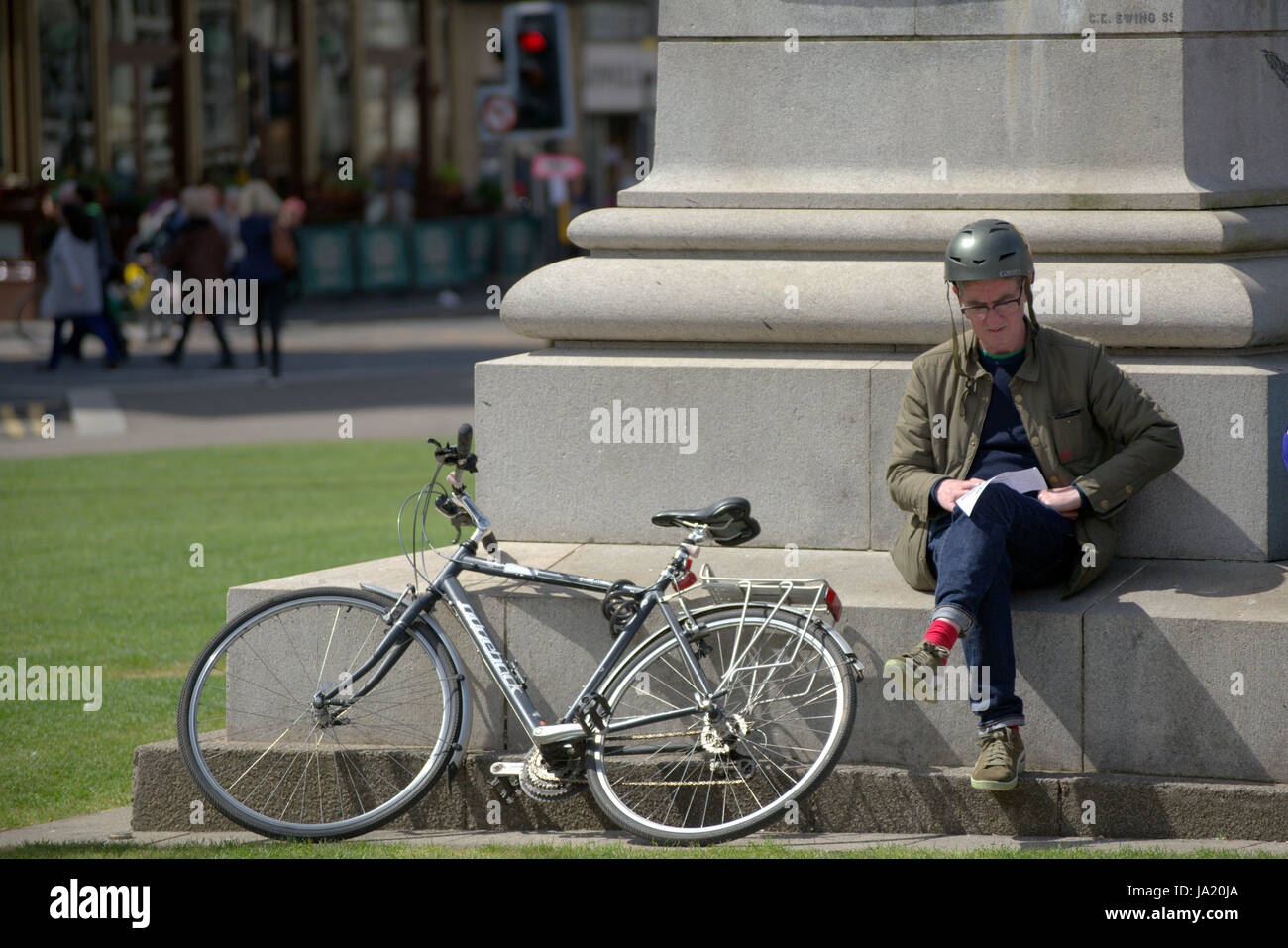 cyclist sitting down reading map with bike against monument in George Square Glasgow Stock Photo