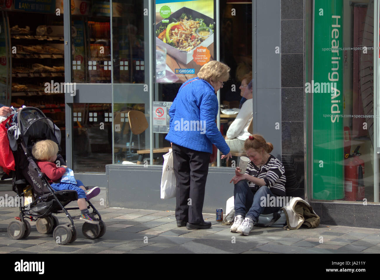 homeless in the uk begging on the street  old lady helping witnessed by child Stock Photo