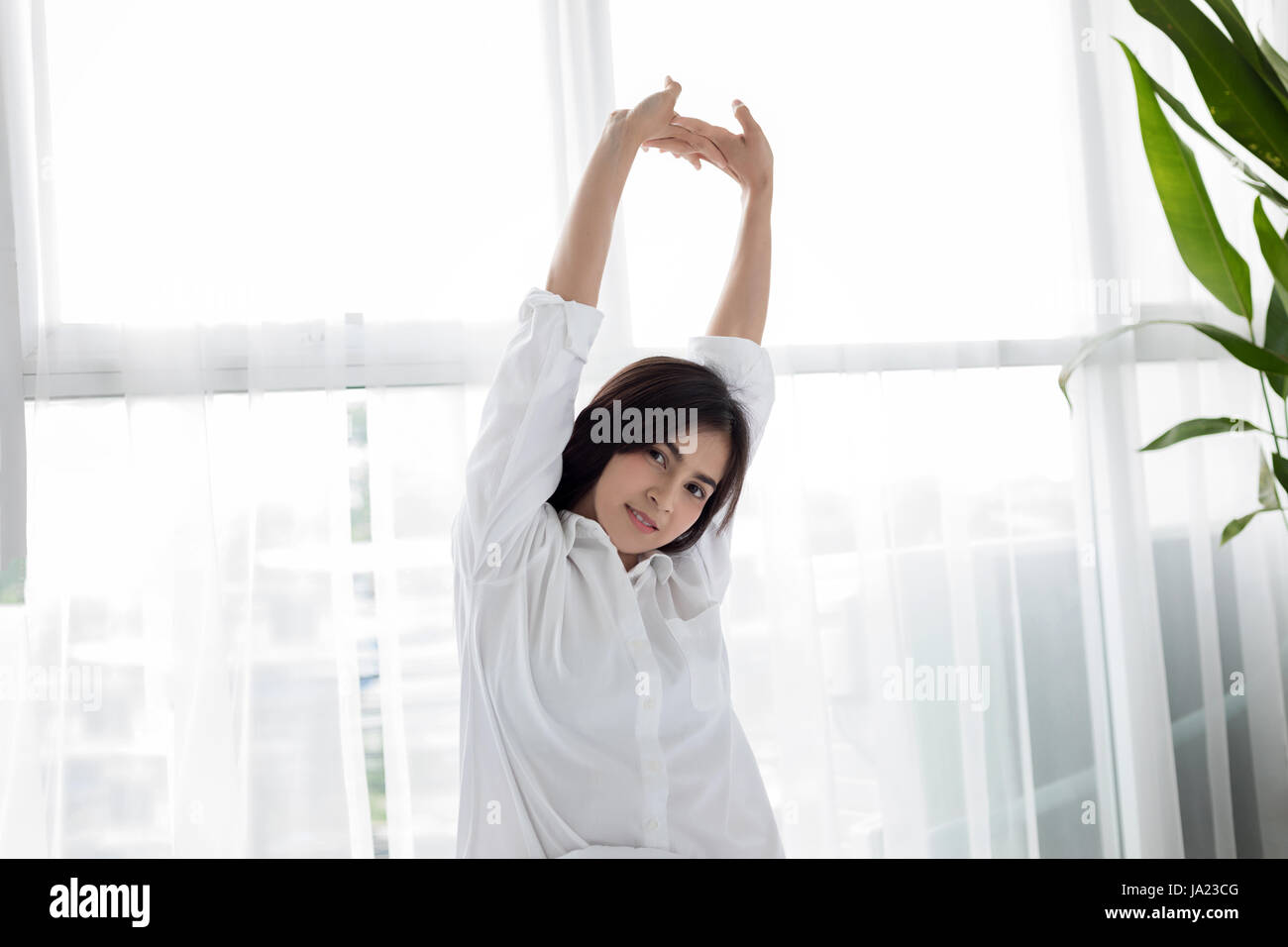 asian-woman-beautiful-young-smiling-woman-sitting-on-bed-and-stretching-JA23CG.jpg